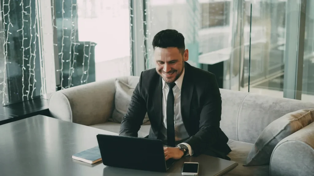 A man in a suit smiling while using a laptop
