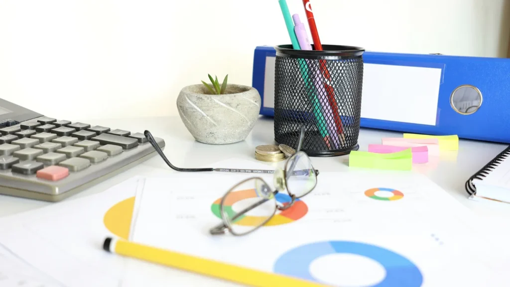 A desk with a calculator, glasses, charts and files