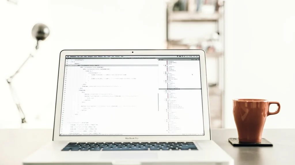 A MacBook Pro on a desk beside a brown mug