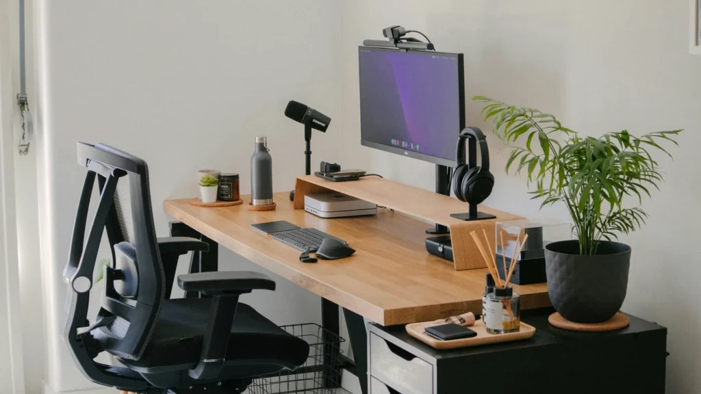 A home office desk with a monitor, office chair and plant